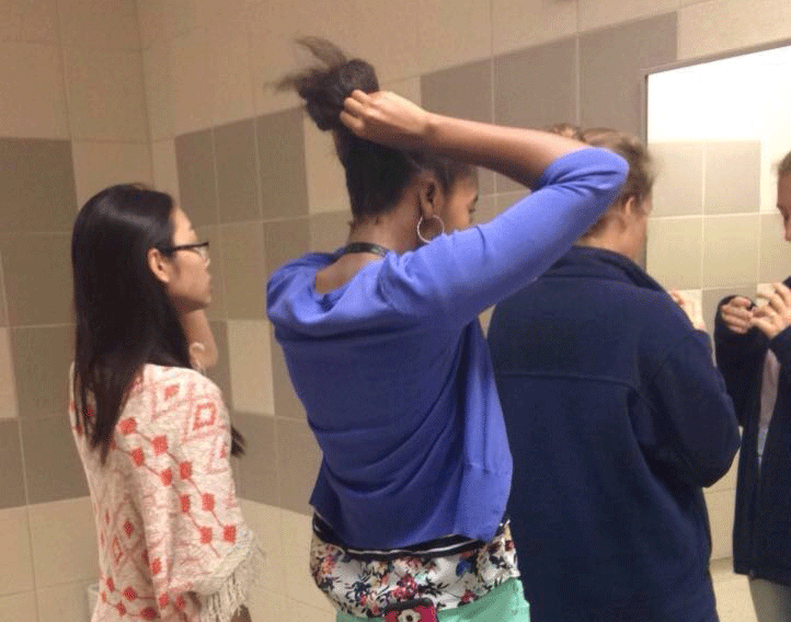Girls try to fix how they look in the bathroom mirror.