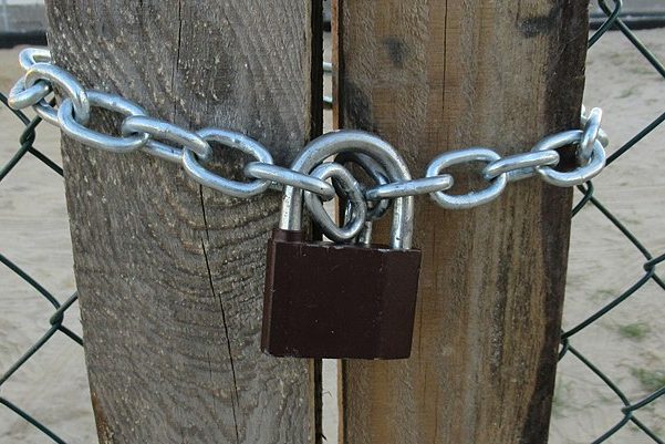 Padlock clipped onto chain and wrapped around wooden posts. Photo courtesy of Grzegorz W. Tężycki, licensed under CC BY-SA 4.0