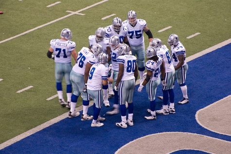 Dallas Cowboys team in a group huddle near the end zone. Cowboys Huddle by Billy Bain is licensed under CC BY 2.0
